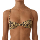 A model wearing a two-piece leopard print bikini with a tan base and black spots, shown from the neck to the upper thighs against a plain white background.